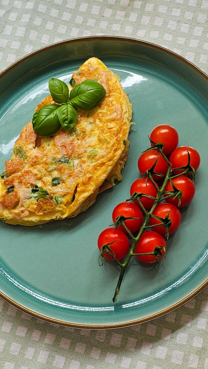 Delicious omelette with basil leaves and fresh cherry tomatoes served on a plate.