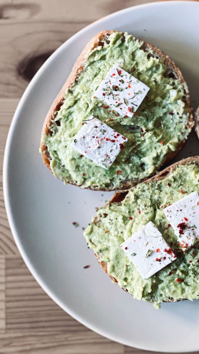 Delicious avocado toast with feta cheese, seasoned with spices, served on a plate.